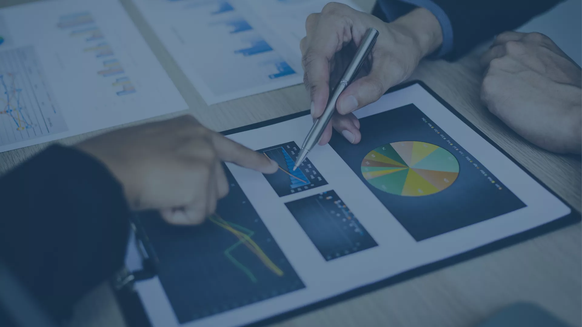 Zwei Personen analysieren gemeinsam Wirtschaftsdaten auf gedruckten Diagrammen und einem Tablet. Ein Kreisdiagramm und zwei Balkendiagramme stehen im Fokus. Der Kontext verweist auf wirtschaftliche Herausforderungen und die Chancen von Förderprogrammen, um digitale Prozesse wie ERP- und CRM-Systeme zu implementieren | audius