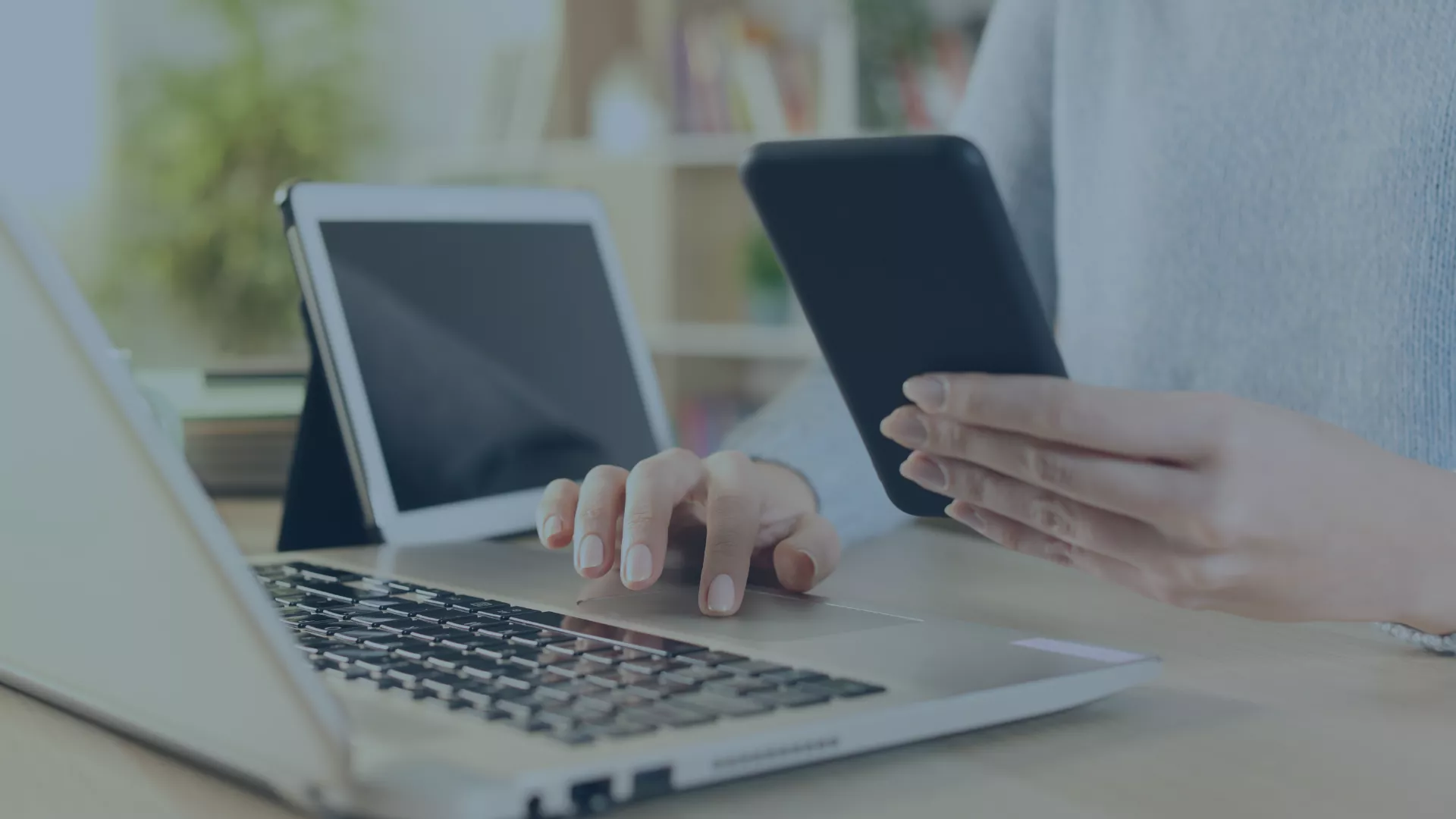 Person arbeitet an einem Laptop, hält ein Smartphone in der Hand und hat ein Tablet im Hintergrund – symbolisch für die plattformübergreifende Verwaltung mobiler Endgeräte mit dem MDM-System Relution, das Datenschutz und Effizienz in Unternehmen und Bildungseinrichtungen vereint.