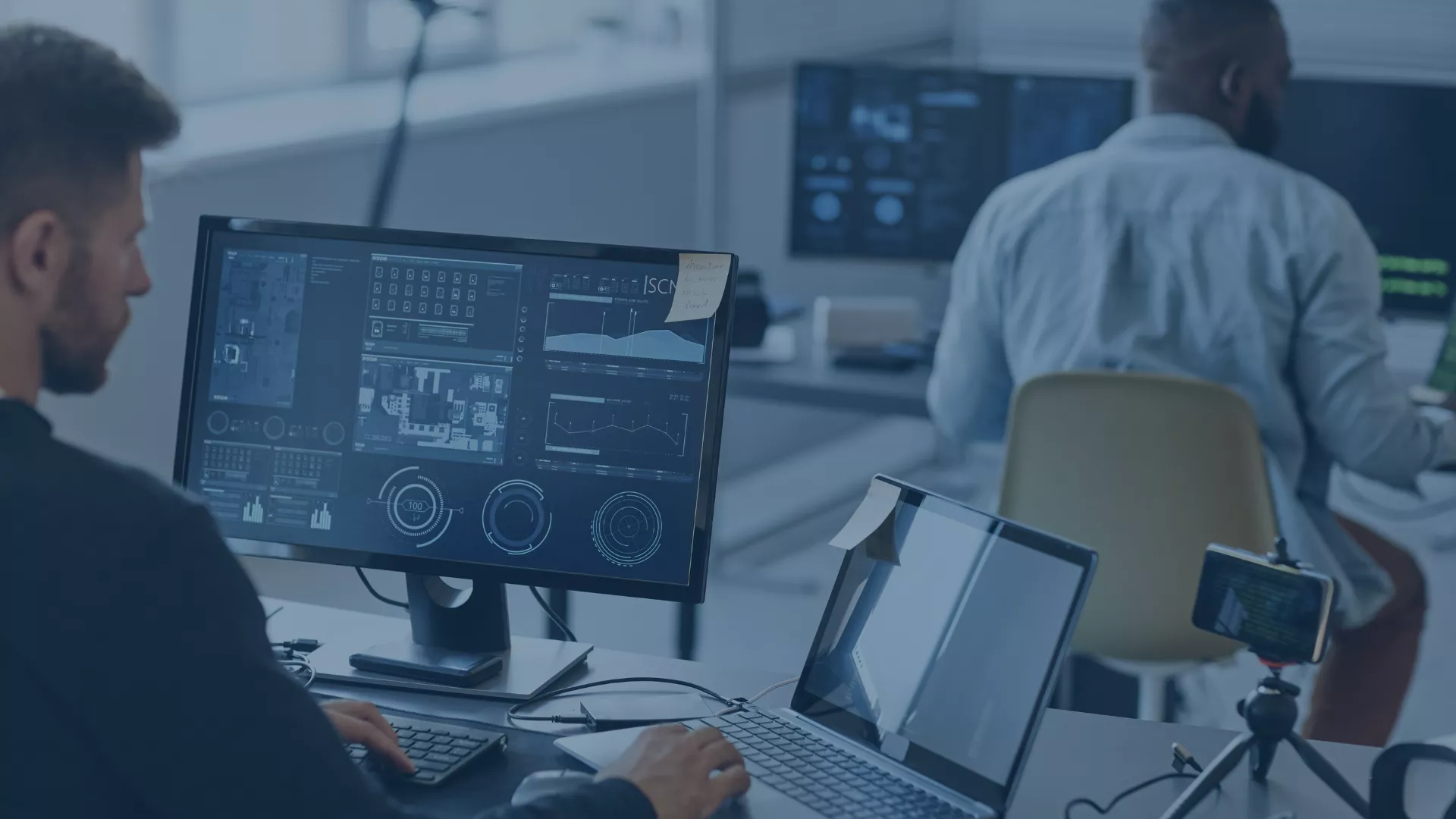 Zwei IT-Mitarbeiter arbeiten an Monitoren mit technischen Dashboards. Symbolisiert, wie audius:Software & Consulting Ordnung, Transparenz und durchgängige Prozesse in IT- und Softwareunternehmen schafft.