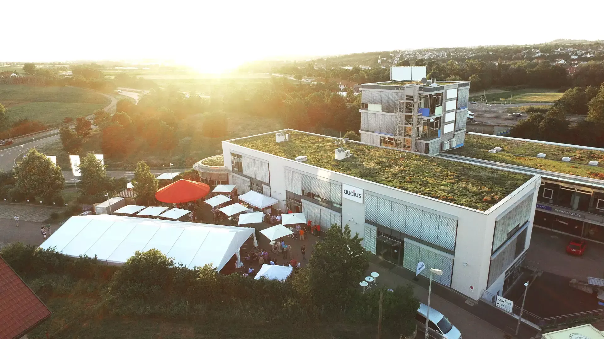 Außenansicht des audius Firmengebäudes in Weinstadt bei Sonnenuntergang mit Firmenevent im Außenbereich und begrüntem Dach.