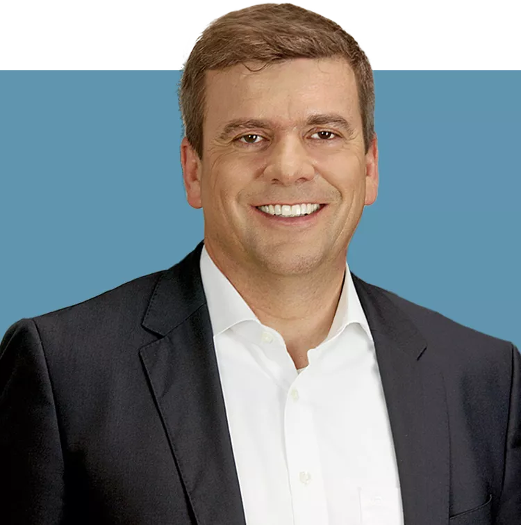Porträt von Rainer Francisi, Vorstandsmitglied der audius SE, lächelnd in dunklem Sakko und weißem Hemd vor blauem Hintergrund.